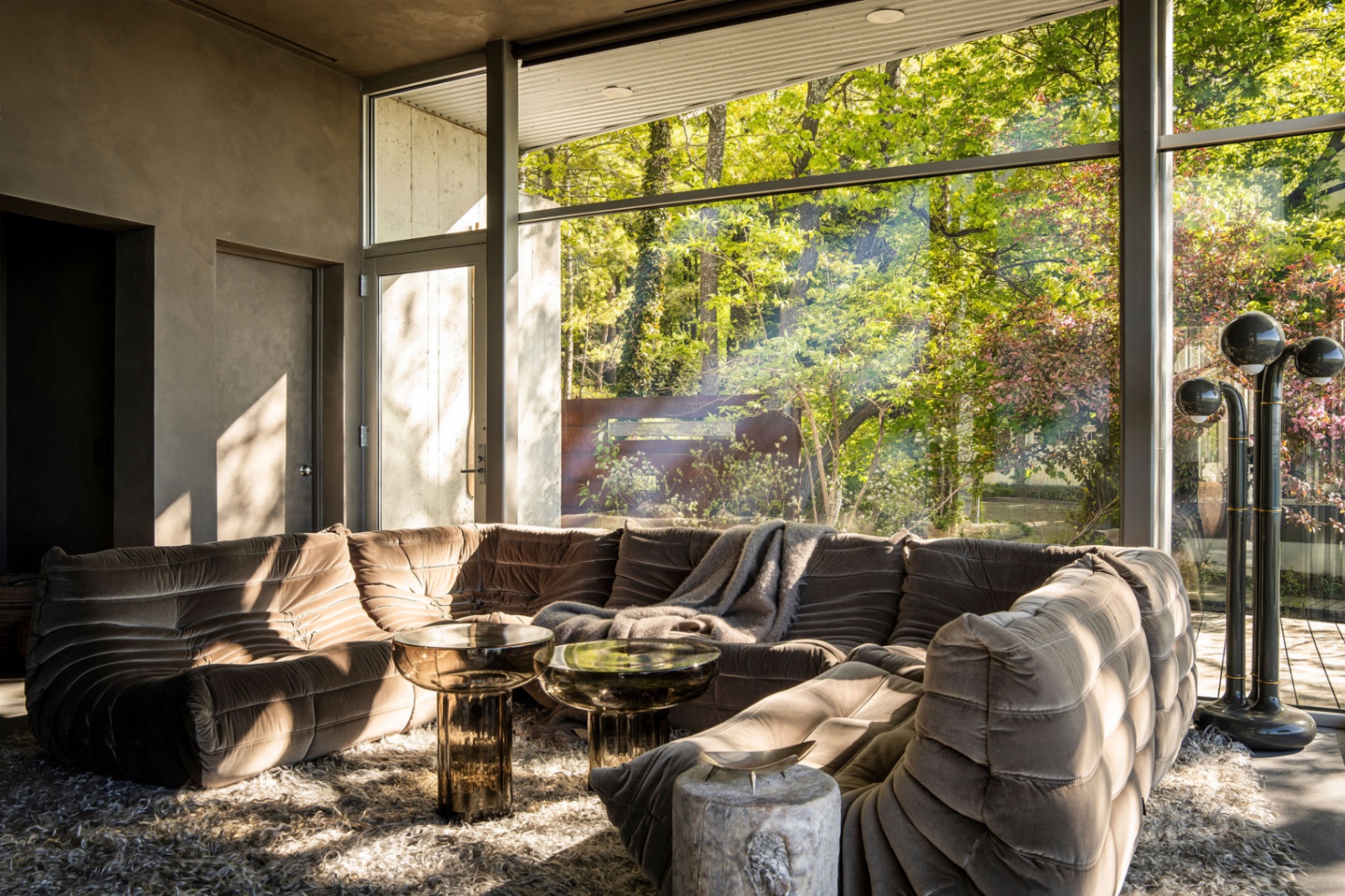 A sunlit modern living room with a sculptural sofa layered over a tonal rug