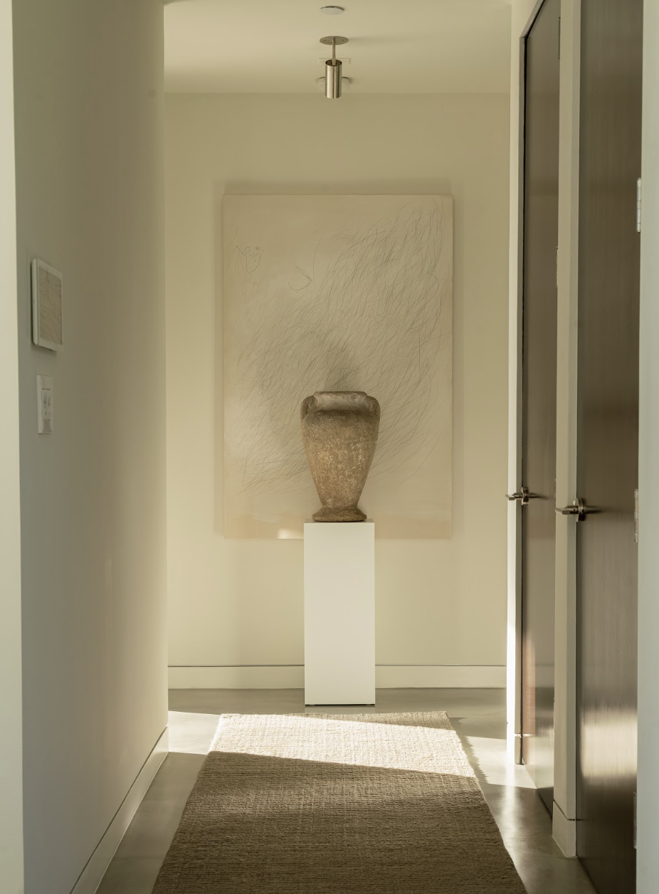 A serene hallway with a handwoven neutral rug, sculptural vessel, and minimalist artwork