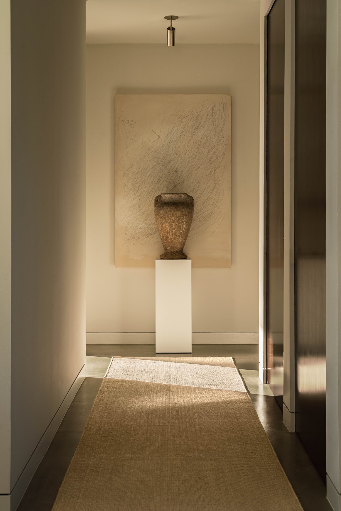 A serene hallway with a handwoven neutral rug, sculptural vessel, and minimalist artwork